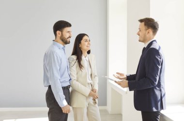 Yeni evde erkek emlakçıyla konuşan ve ev sahibi olmaya hazır bir kadın ve erkek. Profesyonel neşeli emlakçı genç çifte yeni bir daire gösteriyor. Emlak piyasası kavramı.