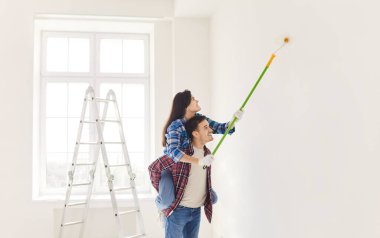 Pozitif aile çiftleri duvar boyuyor ve yeni evlerinin tadilatı sırasında eğleniyorlar. Takım çalışması ve işbirliği, inşaat ve ev iyileştirme görevlerinde ortak bir çabayı gösteriyor.