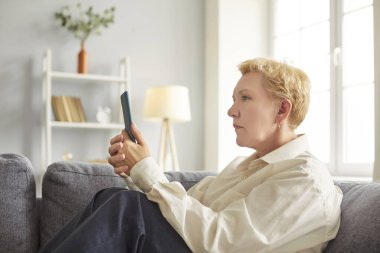 Evde kanepede oturan yaşlı bir kadın, akıllı telefon ekranındaki uygulamaları kullanıyor, olgun bir kadın arkadaşlarıyla ya da çocuklarıyla haberci ya da sosyal ağda sohbet ediyor, internet mağazasından alışveriş yapıyor.