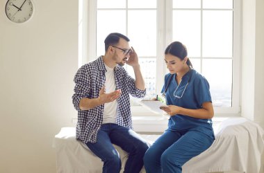 Genç bir hasta muayene sırasında klinikteki kadın hemşireyle konuşuyor. Kanepede oturuyor. Hastaların şikayetlerini dinleyen bir tıp çalışanı. Sağlık hizmetleri kavramı.