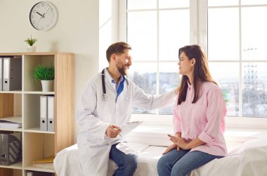 Erkek bir doktorun portresi, elini omzuna koyan gülümseyen genç bir kadın hastaya destek oluyor. Klinikte oturan hekim muayenede bir kadına danışmanlık yapıyor..