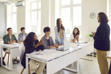 Sınıftaki masada duran genç kız öğrenci ve erkek öğretmene hesap veriyor. Ders sırasında sınıfta çalışan üniversite ya da lise öğrencileri. Eğitim ve öğrenme kavramı.