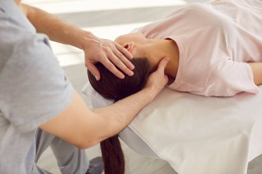 Rehabilitasyon kliniğinde kanepede yatan beyaz bir kadına boyun masajı yapan erkek doktor fizyoterapisti. Fizyoterapi ve osteopatik tıp konsepti.