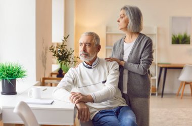 Düşünceli yaşlı çift pencereden uzaklığa bakarken karar vermeyi düşünüyor. Erkek oturur ve pencereden dışarı bakar ve kadın arkasında durur, elini omzunda tutar..