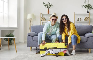 Evli çift birlikte bavul hazırlıyor, yaz tatiline hazırlanıyorlar. Takım çalışmaları ve heyecanları seyahat, tatil ve hafta sonu kaçamağı beklentilerini vurguluyor..