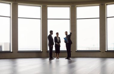 Profesyonel erkek emlakçı temsilcisi, resmi kıyafetler giyen genç ve neşeli iş adamlarına kira için boş modern ofis alanı gösteriyor. Emlak piyasası kavramı.