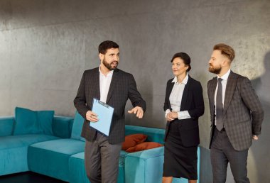 Genç ve neşeli iş adamları modern ofiste erkek partnerle ya da emlakçıyla kontratı tartışıyorlar. İçerde çalışan kendine güvenen şirket çalışanları grubu..