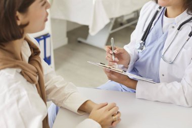 Klinik ziyareti sırasında tıbbi belgeleri dolduran doktor, kadın doktor hastayla konuşuyor, reçeteyi açıklıyor, tıbbi tarama, muayene sonucu, danışmanlık yapıyor.