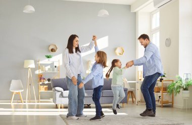 Evde mutlu aile eğlenceleri, modern sıcak oturma odasında küçük çocuklarla dans eden ebeveynler, yeni eve taşınmak, banka kredilerini ve kredileri, eğlenceleri, çocuklarla eğlenmeyi kutlamak.