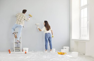 Genç çift yeni dairelerinin iç duvarlarını boyuyor, ellerinde boya ruloları ve merdiven kullanıyorlar. Evli bir adam ve kadın tadilat yapıyor ve yeni evlerine taşınmaya hazırlanıyorlar..