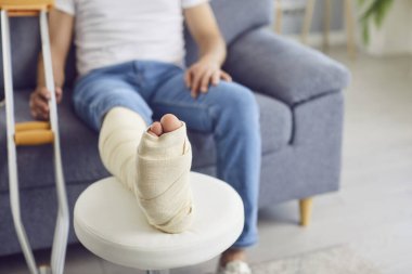 Ayağı alçıda sakat bir adamın rehabilitasyonda kanepede oturması ve kırık uzuvlarının iyileşmesi. Seçici odaklanma. İyileşme ve rehabilitasyon konsepti.