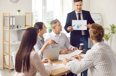 İş adamı, ofiste iş ekibiyle bir toplantı ya da konferans düzenler, belgelerle uğraşır. Grup etkili iletişim ve organizasyonel sohbete girişir..