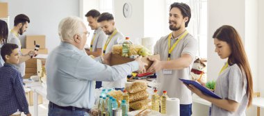Hayır kurumunda gönüllülerden oluşan bir ekiple birlikte çalışan ve yardıma ihtiyacı olanlara hayır kurumunda bedava yiyecek bağışlayan neşeli genç bir adam. İnsani yardım ve gönüllü yardım kavramı. Pankart.