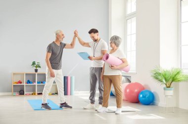 Rehabilitasyon merkezindeki yaşlı çift antrenörle konuşuyor. Mutlu yaşlılar eğitimden sonra eğitmene teşekkür eder. Mutlu kıdemli kavramı, egzersiz, özen, fiziksel egzersiz