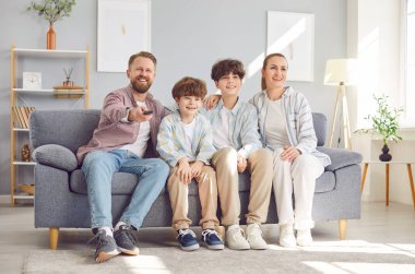 Evdeki kanepede oturup televizyon izleyen dört çocuklu mutlu ailenin portresi. İki oğlu olan ebeveynler futbol takımını destekliyor ya da birlikte komik film izliyorlar..