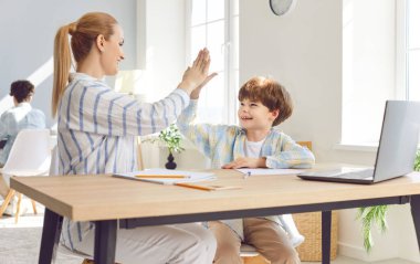 Anne oğluna ödevlerinde yardım ediyor ve yardım ediyor, onlar da beşlik çakıyor. Bir aile olarak bir anne ve oğul arasındaki destekleyici ve eğitici bağ, takım çalışmasının altını çizmek ve öğrenmeyi teşvik etmek.