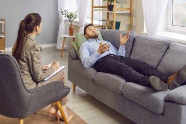 Yetişkin bir hasta psikoterapist ya da klinik psikologla konuşuyor. Genç bir adam terapi seansı yapıyor, kanepeye uzanıyor, sorunları uzmanla paylaşıyor, tavsiye istiyor. Psikoterapi kavramı