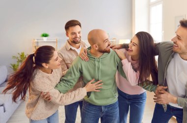 Mutlu gülümseyen komik arkadaşlar ya da günlük kıyafetler giymiş meslektaşlar oturma odasında durup gülüyorlar. Genç arkadaş canlısı erkekler ve kızlar evde sarılıyor. Ev partisinin tadını çıkarıyorlar..