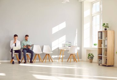 Genç iş adamları dizüstü bilgisayarları ve dizüstü bilgisayarlarıyla koltuklarda oturuyorlar. Ofiste çalışan bir grup personel ve şirket çalışanı. İş başvurusunda bulunanlar görüşme daveti bekliyorlar