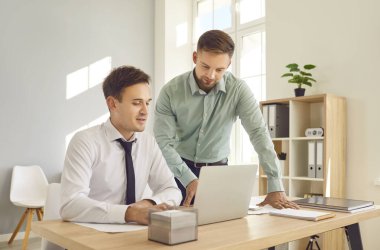 İş yerindeki işadamları. İki genç kendine güvenen işveren toplantı masasında oturmuş dizüstü bilgisayar ekranına bakıyor yeni projeleri ya da girişimleri tartışıyor, şirketi analiz ediyor..