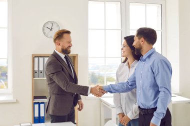 Erkek banka çalışanı, başarılı bir anlaşma imzalayıp işbirliğine başladıktan sonra evli çiftle tokalaşıyor. Sigorta acentesi ya da tefeciyle aile danışmanlığı. İş ahlakı kavramı.