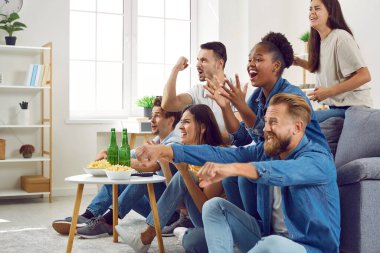 Televizyonda futbol izleyen bir grup genç erkek ve kadın arkadaş. Bir grup mutlu karışık ırk hafta sonunun tadını çıkarıyor, kanepede oturup futbol seyrediyor ve tezahürat yapıyorlar.