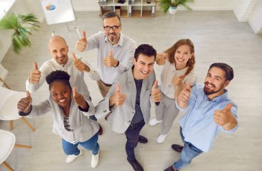 Bir grup mutlu iş arkadaşı ya da memnun müşteri iyi hizmet için tavsiye veriyor. Ofisteki çok ırklı insanların üst görüşü, desteklerini ve onaylarını başparmak hareketiyle gösteriyor..