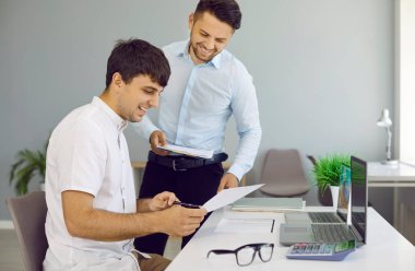 Takım çalışması ve ortaklık. Neşeli meslektaşlar ofiste çalışırken kağıt dökümanları inceliyor ve tartışıyorlar. Elinde belgeleri olan ve konuşan iki genç adam. Yan görünüm.