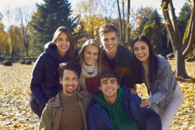 Sonbahar parkında yürüyen bir grup mutlu arkadaşın portresi. Genç beyaz insanlar, kızlar ve oğlanlar kameraya bakıyor ve dışarıda neşeli bir şekilde gülümsüyorlar. Arkadaşlık ve birliktelik kavramı.