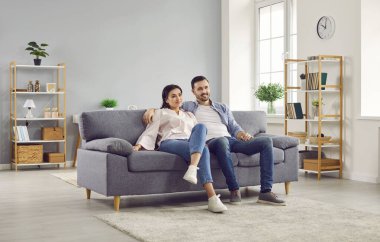 Çift oturma odasında kanepede otururken birlikte televizyon izliyor. Neşeli eşler rahat koltukta oturup televizyon seyrediyorlar. Mutlu aile evde birlikte vakit geçiriyor.