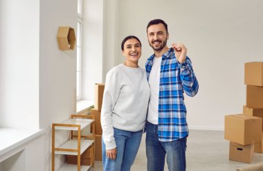 Yeni evde kameranın anahtarlarını gösteren mutlu aile çifti. Gülümseyen eşler, oturma odasında karton kutularla bekleyen ev sahipleri, yeni bir eve taşınan çiftler. Taşınma günü, emlak konsepti.