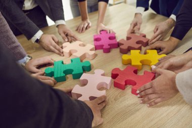 Çok renkli yapboz yapan bir grup iş adamının kırpılmış elleri. İşbirliği, takım çalışması, yardım ve destek kavramı. İş arkadaşları yapboz parçalarına ofiste katılırlar. Üst görünüm.