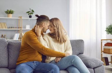 Sevgi dolu çift burunlarına dokunuyor ve evde sarılıyorlar. Mutlu adam ve kadın sıcak örülü kazaklar içinde kanepede otururken birbirlerine şefkatle bakıyorlar. Aşk, ilişki, romantik konsept