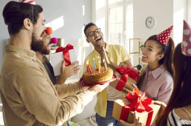 Mutlu farklı arkadaşlar, doğum günü hediyesi olan heyecanlı kızı kutlayın ve mumlarla pasta yapın. Gülümseyen çok ırklı gençler, bayanları yıldönümleriyle selamlıyor. Kutlama konsepti.