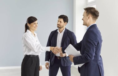 Ofiste bir kadın bir erkekle tokalaşıyor, yakın plan. Bir grup iş adamı içeride. İşyerine yeni bir çalışanı kabul etme kavramı. Seçilen pozisyon için aday, iş ortaklığı