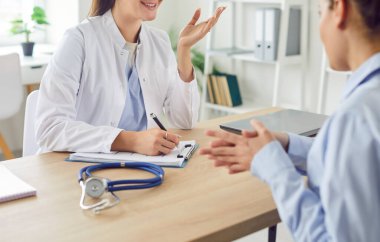 Gülümseyen genç kadın konuşması, kadın hasta toplantıda doktor terapisti dinlemesi, hastanede masada oturması, doktora muayene sonuçları hakkında danışması, tavsiye vermesi, yazı yazması.