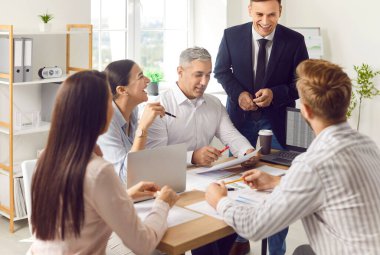 Mutlu iş adamları toplantı ya da brifing sırasında ofiste birlikte çalışırlar. Konuşmada başarılı ve kendinden emin grup, etkili iletişim ve işbirliğini vurguladı.