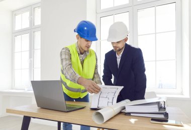 Genç bir erkek mimar, iç mimar ustabaşı inşaat projesiyle inşaat alanında çalışma projesini tartışıyor. Mimari planın mühendis teftişi.