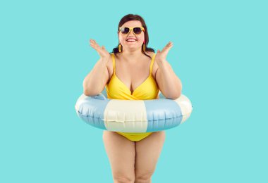 Mutlu şişman tombul kadın portresi. Sarı yaz tatili mayosu, güneş gözlüğü ve çizgili plaj yüzüğü takan. Mavi arka planda duruyor, gülümsüyor ve alkışlıyor.