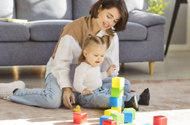 Evde ya da bebek bakıcısının öğrendiği mutlu genç anne, bebeklere oyuncak kuleler inşa etmede yardım etmek, tahta inşaat blokları, sıcak, özenli bir bakıcıyla oynayan anne, çocuklara bakıcılık yapan çocuk. 