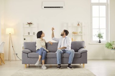 Evli çift evdeki klimayı iklimi kontrol etmek için ayarlıyor. Odayı ısıtmak ya da soğutmak için klimayı açarak evlerini uygun sıcaklıkta tutarak rahatlığı sağlıyorlar..