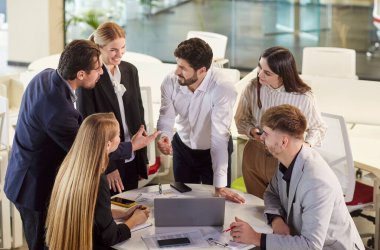 Modern ofiste masa etrafında iş birliği yapan bir grup iş adamı. Üretken toplantı sırasında fikirleri ve stratejileri tartışan, görüşleri paylaşan ve verileri analiz eden kendinden emin bir ekip.