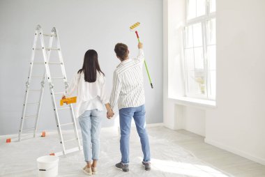 Yeni evlerinin duvarına bakıp duvarları boyamayı tartışan genç bir aile manzarası. Mutlu karı koca plan yapıyor, tadilat ve dekorasyon yapıyor..