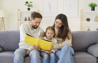 Sevgi dolu, pozitif ebeveynler ve küçük kız evde birlikte kitap okuyarak güzel bir gün geçiriyorlar. Bağ kurma etkinliği öğrenmeyi, aile birliğini ve değerli bağlantı anlarını teşvik eder..