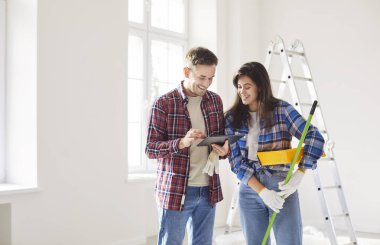 Mutlu genç evli çift tabletleri ev yenileme eğlencesinin tadını çıkarıyor, yeni eve taşındıktan sonra tamir ediliyor, ev sahipleri, kiracılar, erkek, kadın duvar boyası, şakalaşma, gülme, birlikte keyif alma.