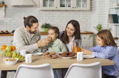 Ebeveynler ve çocuklar evde bir tatil kutlarken gülüyorlar. Mutfaktaki yemek masasında birlikte oturan aile, neşeli ve neşeli bir günde yemek, neşe ve beraberliğin tadını çıkarıyor..