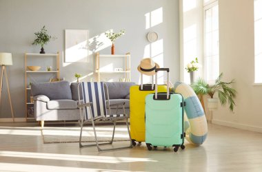 Renkli bavullar, şezlong, ve evdeki boş bir odada kauçuk yüzük standı, bavulları simgeliyor, yaz tatiline hazırlık. Seyahat heyecanı ve yolculuk beklentisi.