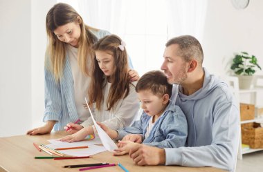 İlgili ebeveynler ve iki çocukları masada oturup, resim çizip, resim yapıyorlar. Yaratıcı görev yerine mutlu aile bağları, renkli kalemler kullanarak evde güzel vakit geçirmek ve resim yapmak..