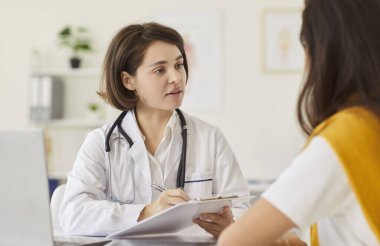 Klinikteki genç kadın pratisyen doktor hasta kadınla konuşuyor, check-up sonuçlarını, sağlık taramasını, randevu muayenesini, hastane ziyaretini, tavsiyesini anlatıyor.