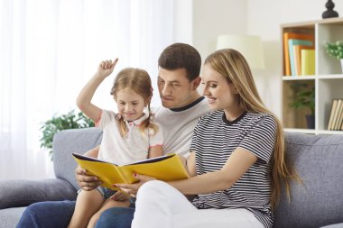 Mutlu ve sevgi dolu bir aile evde kitap okumayı sever. Genç baba, anne, küçük tatlı kızları olan genç anne, baba, küçük çocuk masalları anlatan, kanepede oturan 